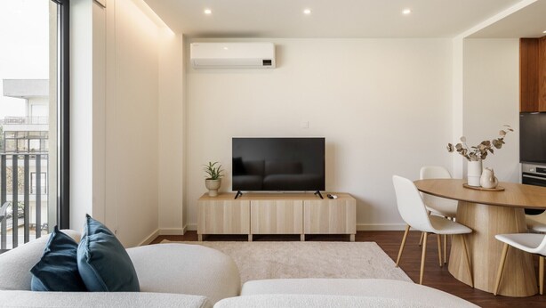 A modern living room with a flat-screen TV on a wooden console, a dining area with a round table, and a balcony with outdoor furniture. - 196 Andrade Corvo Collection by Minhos Guest (Braga)