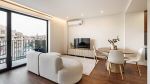 A modern living room with a sofa, a dining table with chairs, a TV, and a large window offering a city view. - 196 Andrade Corvo Collection by Minhos Guest (Braga)