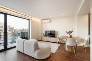 A modern living room with a sofa, a dining table with chairs, a TV, and a large window offering a city view. - 196 Andrade Corvo Collection by Minhos Guest (Braga)