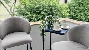 Un balcon avec deux chaises et une petite table, une plante en pot et une tasse.