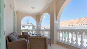 A balcony with wicker furniture, a table, and a railing. - Villa Kallia (Spetses)