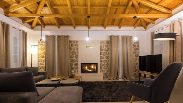 A cozy living room with a fireplace, wooden ceiling beams, and modern furniture. - Villa Kallia (Spetses)