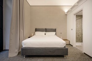 Een moderne hotelkamer met een groot bed, een nachtkastje en een deur naar de badkamer.