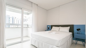 Una camera d'albergo moderna con un letto grande, un comodino, una lampada e vista sulla città attraverso una grande finestra.