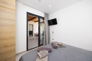 Un dormitorio moderno con cama, televisor de pantalla plana y puerta corrediza de vidrio que da a un balcón.