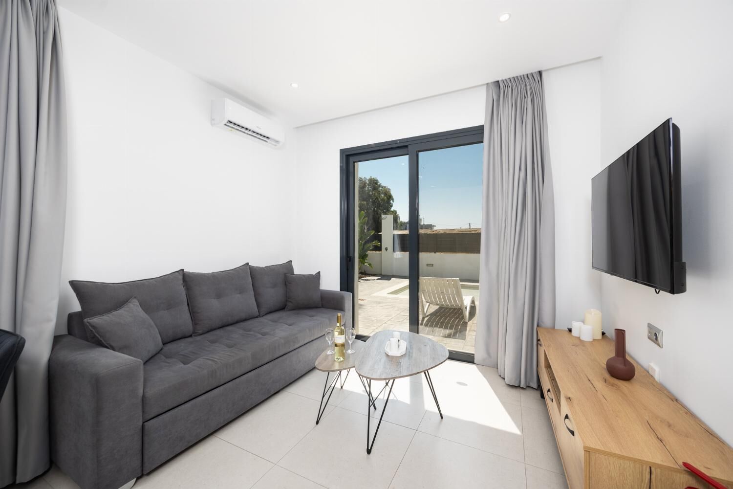 A modern living room with a grey sofa, a small round table, and a TV mounted on the wall.