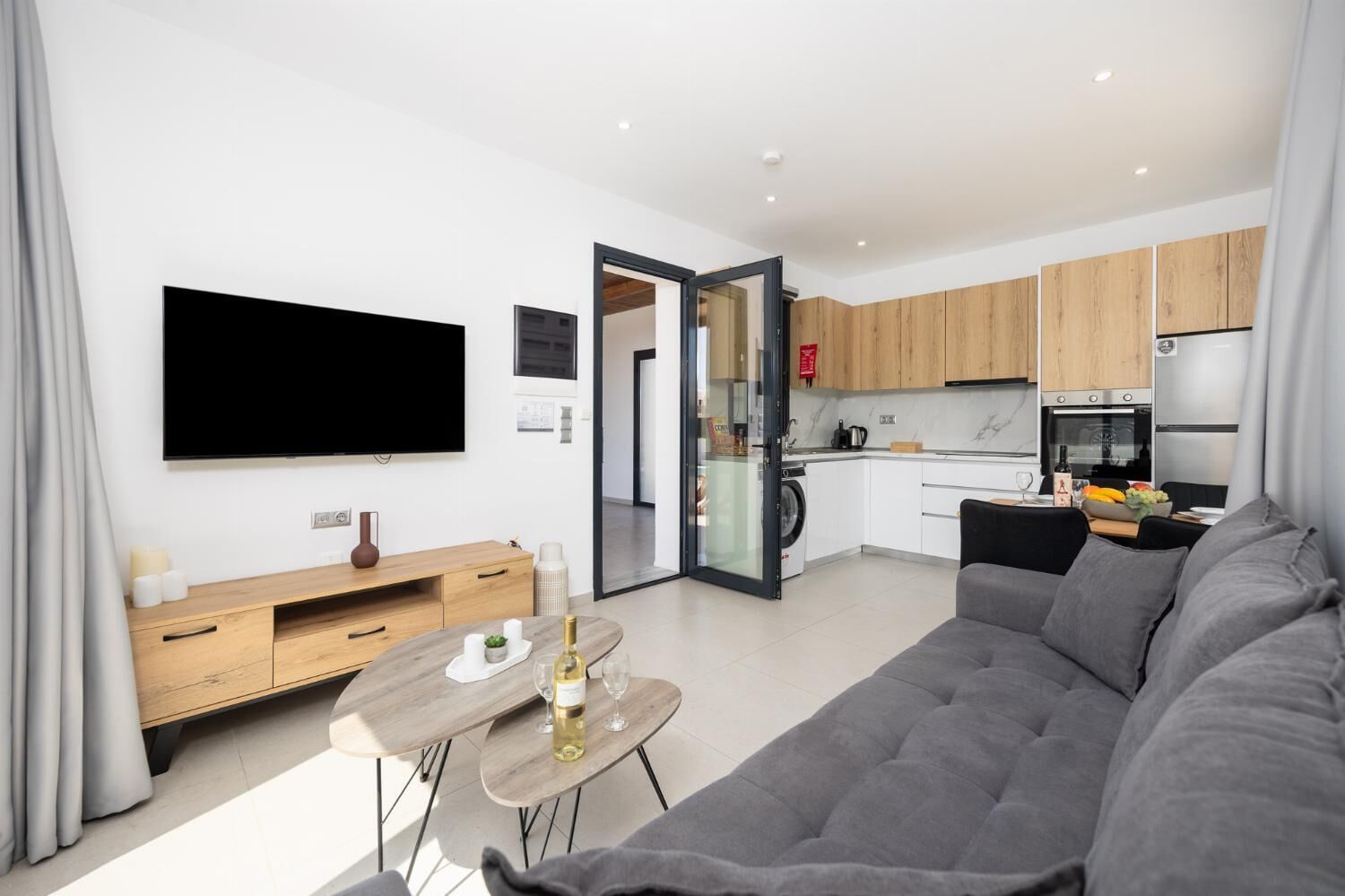 Un salon moderne avec un canapé gris, une table basse en bois et un téléviseur à écran plat fixé au mur.