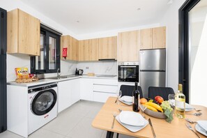 Una cocina moderna con lavadora, una mesa de comedor dispuesta con platos, cubiertos y un frutero.