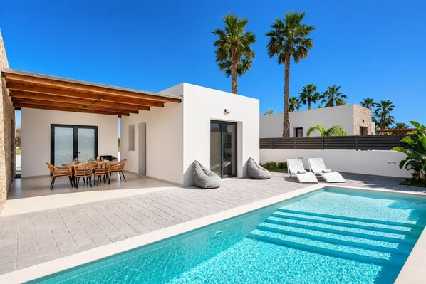 Un espace moderne aménagé au bord de la piscine, comprenant une piscine, des chaises longues et un coin repas.