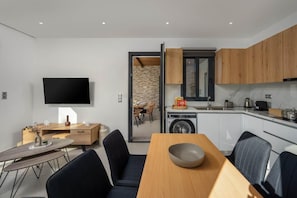 A modern kitchen with wooden cabinets, a built-in washing machine, and a dining area with a wooden table and chairs. - Villa Salty Sun 7 - Two Bedroom Villa, Sleeps 4 (Kremasti)