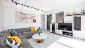 Een moderne woonkamer met een grijze hoekbank, een ronde salontafel, een flatscreen televisie en een trap naar een hoger niveau.