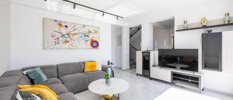 A modern living room with a grey sectional sofa, a round coffee table, a flat-screen TV, and a staircase leading to an upper level.