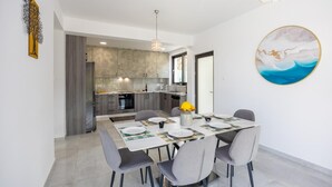 Een moderne keuken met grijze kastjes, een eethoek met een tafel voor vier personen, en een groot abstract schilderij aan de muur.
