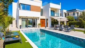 Een modern huis met twee verdiepingen, een zwembad, terras en een verzorgde tuin.