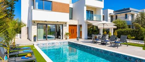 Et moderne hus med to etager, swimmingpool, udendørs møbler og en velplejet have.
