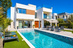 Ein modernes, zweistöckiges Haus mit Schwimmbad, Gartenmöbeln und einem gepflegten Garten.