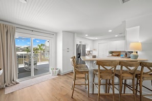A modern kitchen with white cabinets, a central island with bar stools, and a view to an outdoor deck.