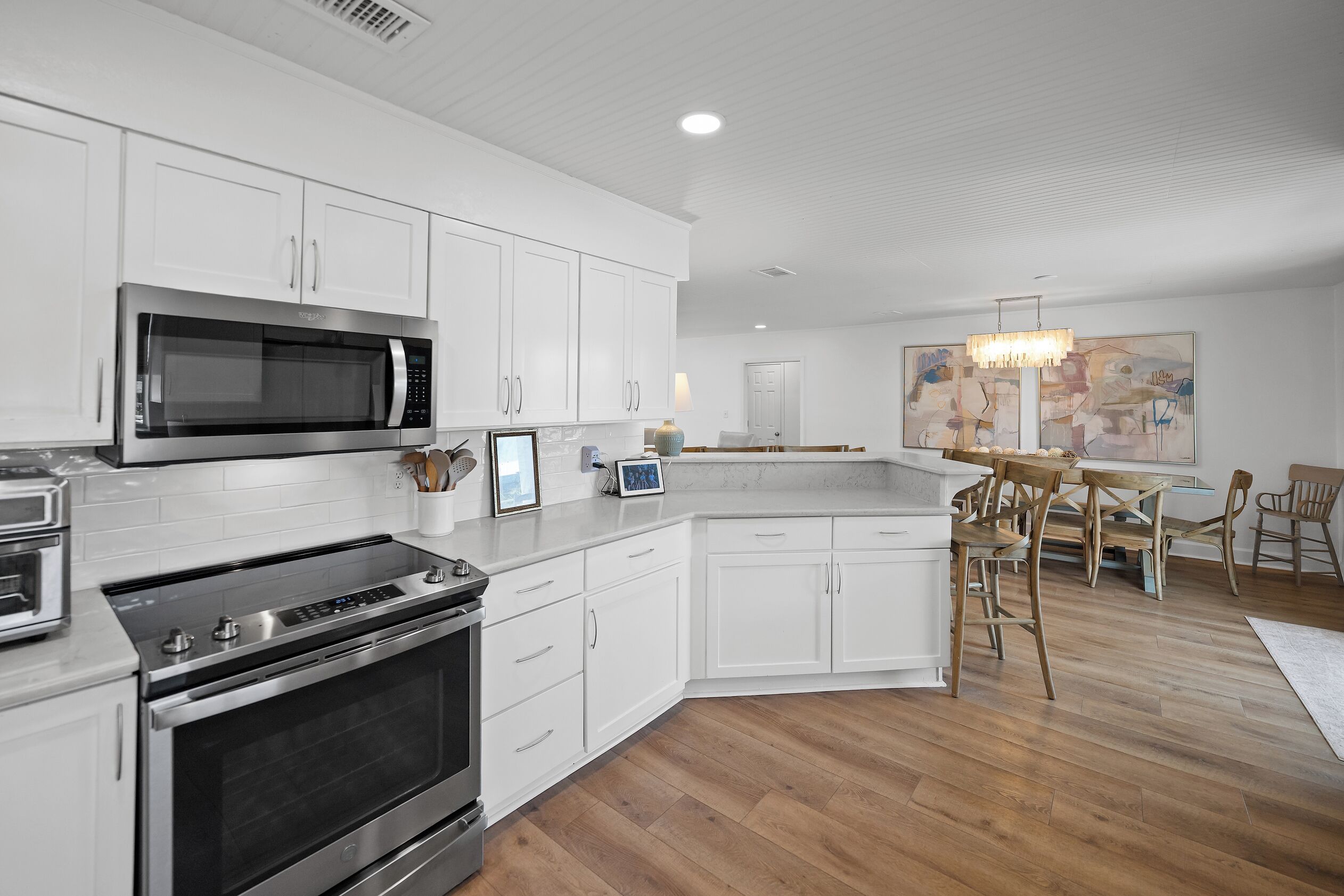 A modern kitchen with white cabinetry, a built-in microwave, a stove, and a dining area with a chandelier.