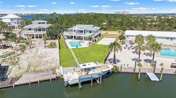 A waterfront property with a large house, a swimming pool, and a boat docked at the pier.