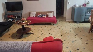 Uma sala de estar com sofá, televisão, mesinha e armário.