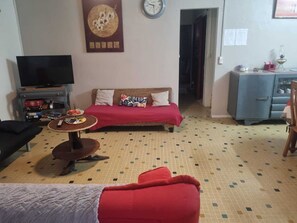 Ein Wohnzimmer mit einer Couch, einem Fernseher, einem kleinen Tisch und einem Schrank.