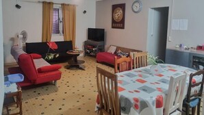 Uma sala de estar com sofá, televisão, mesa de jantar e relógio na parede.