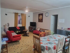 Ein Wohnzimmer mit einer Couch, einem Fernseher, einem Esstisch und einer Wanduhr.