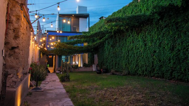Un patio con un edificio moderno, luces colgantes y un seto verde.