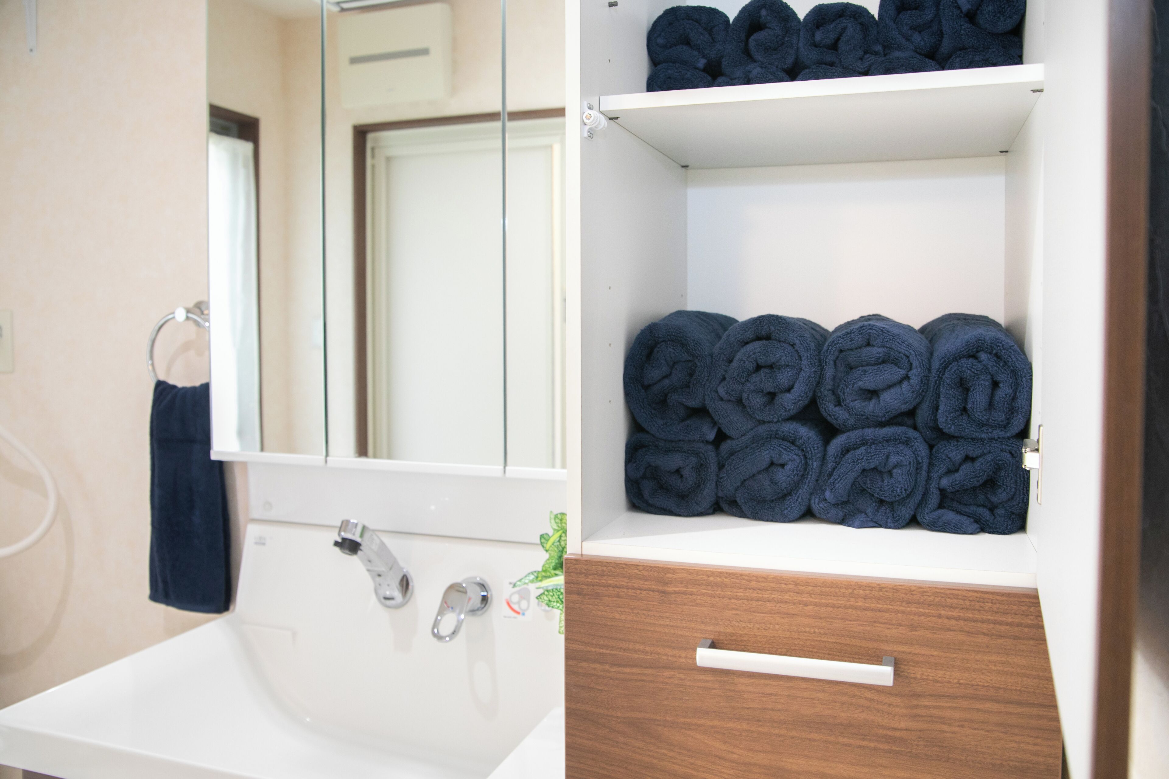 A bathroom with a white sink, a mirror, and shelves holding rolled towels.
