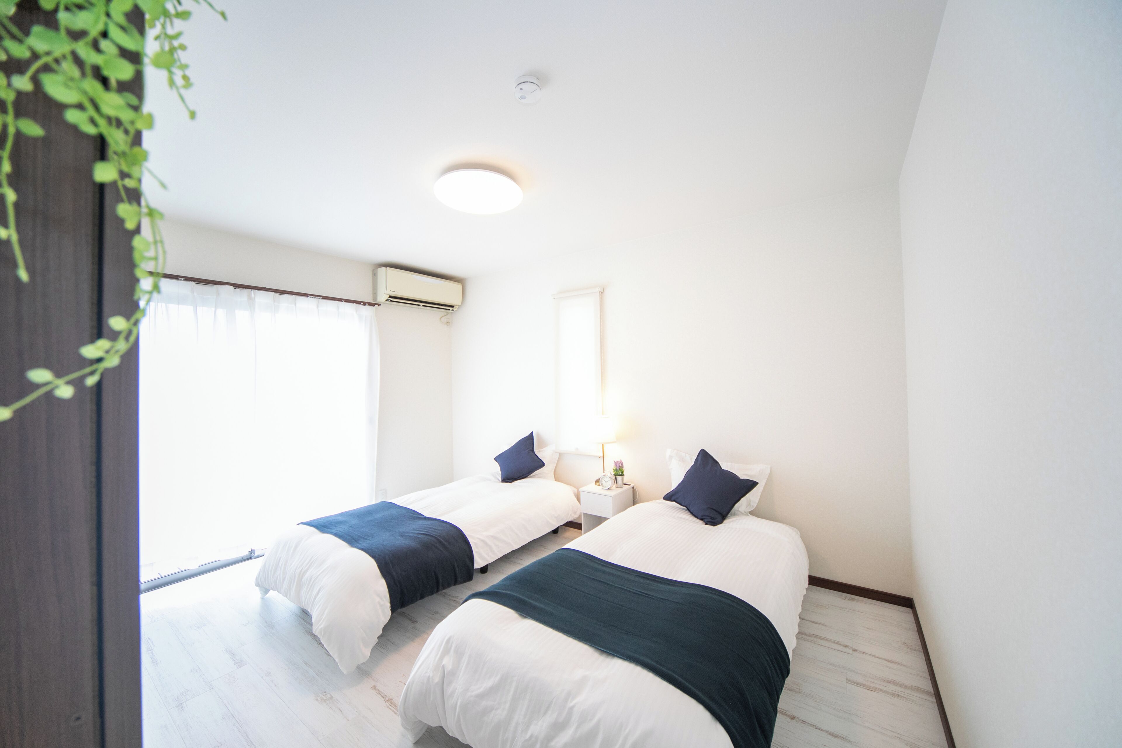 Une chambre avec deux lits, une table de chevet avec une lampe, une fenêtre avec des rideaux et un luminaire au plafond.