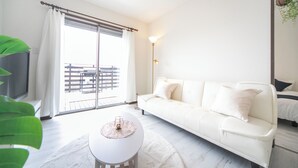 A modern living room with a white sofa, a round coffee table, and a large window with a view of a balcony.