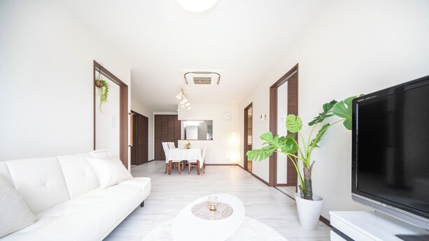 A modern living room with a white sofa, a flat-screen TV, a dining area with a table and chairs, and a potted plant.