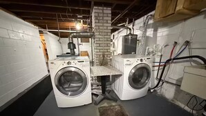 A laundry room with two front-loading washing machines, a metal vent, and a brick wall.