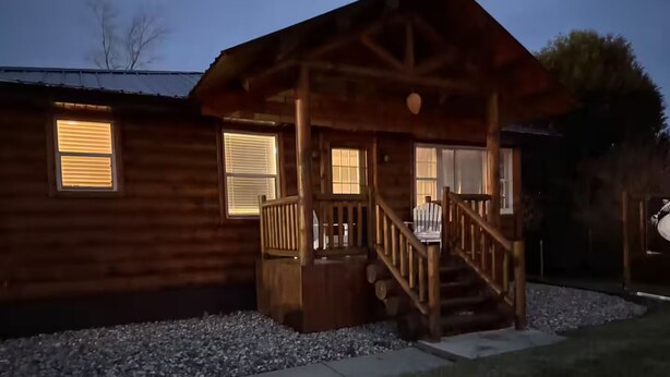 A wooden cabin with a porch, a staircase, and a window with blinds.
