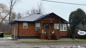 A wooden cabin with a porch, a signboard, and a gravel driveway.