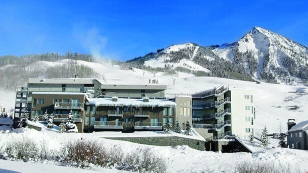 A multi-story hotel with balconies, situated in a snowy mountainous area. - Cozy Condo | Stunning Mountain Views + Fireplace (Crested Butte)