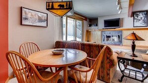 A cozy living room with a round wooden table and chairs, a patterned sofa, and a television on the wall. - Cozy Condo | Stunning Mountain Views + Fireplace (Crested Butte)