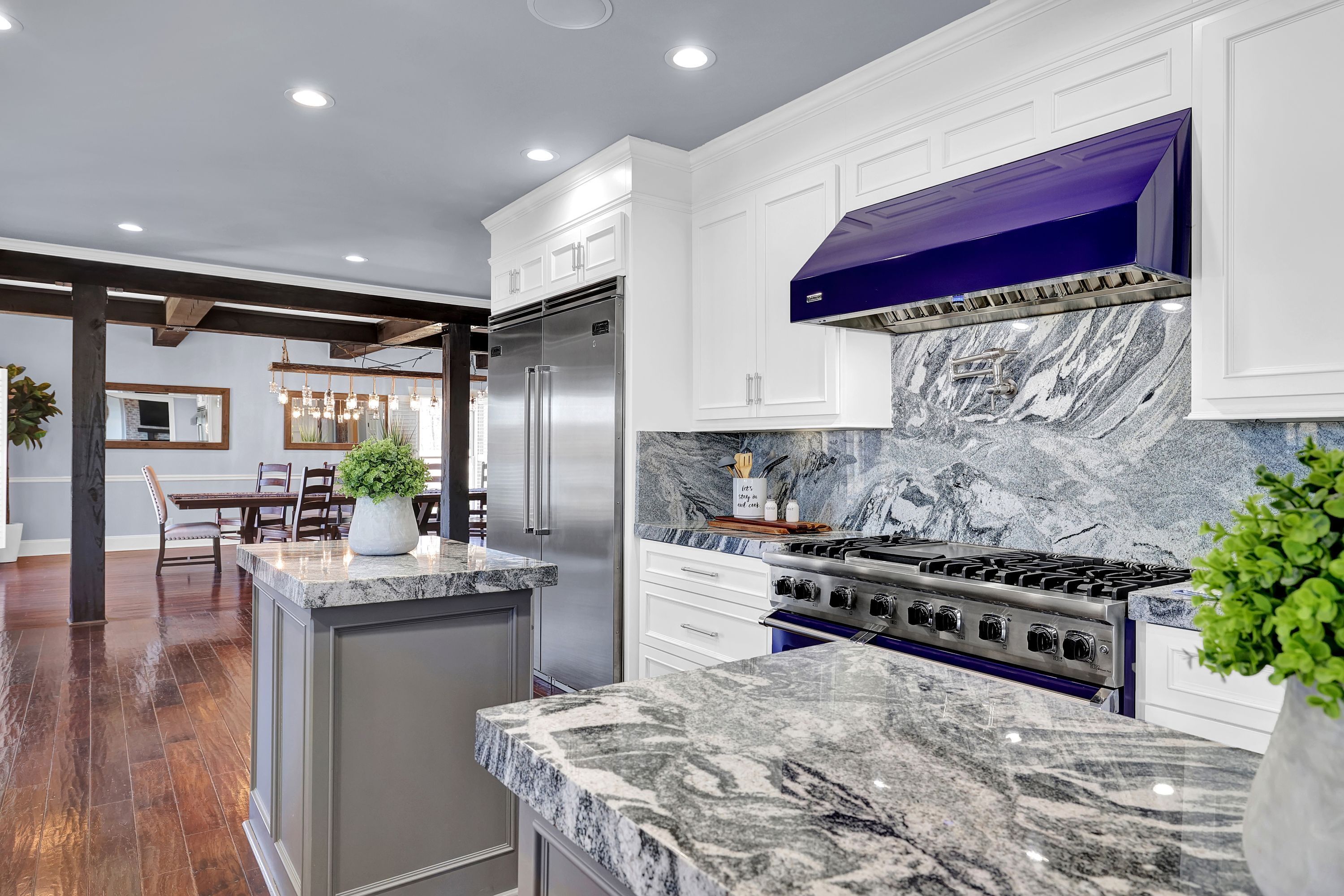 Una cocina moderna con armarios blancos, un refrigerador de acero inoxidable, una campana extractora azul y un protector contra salpicaduras de mármol.