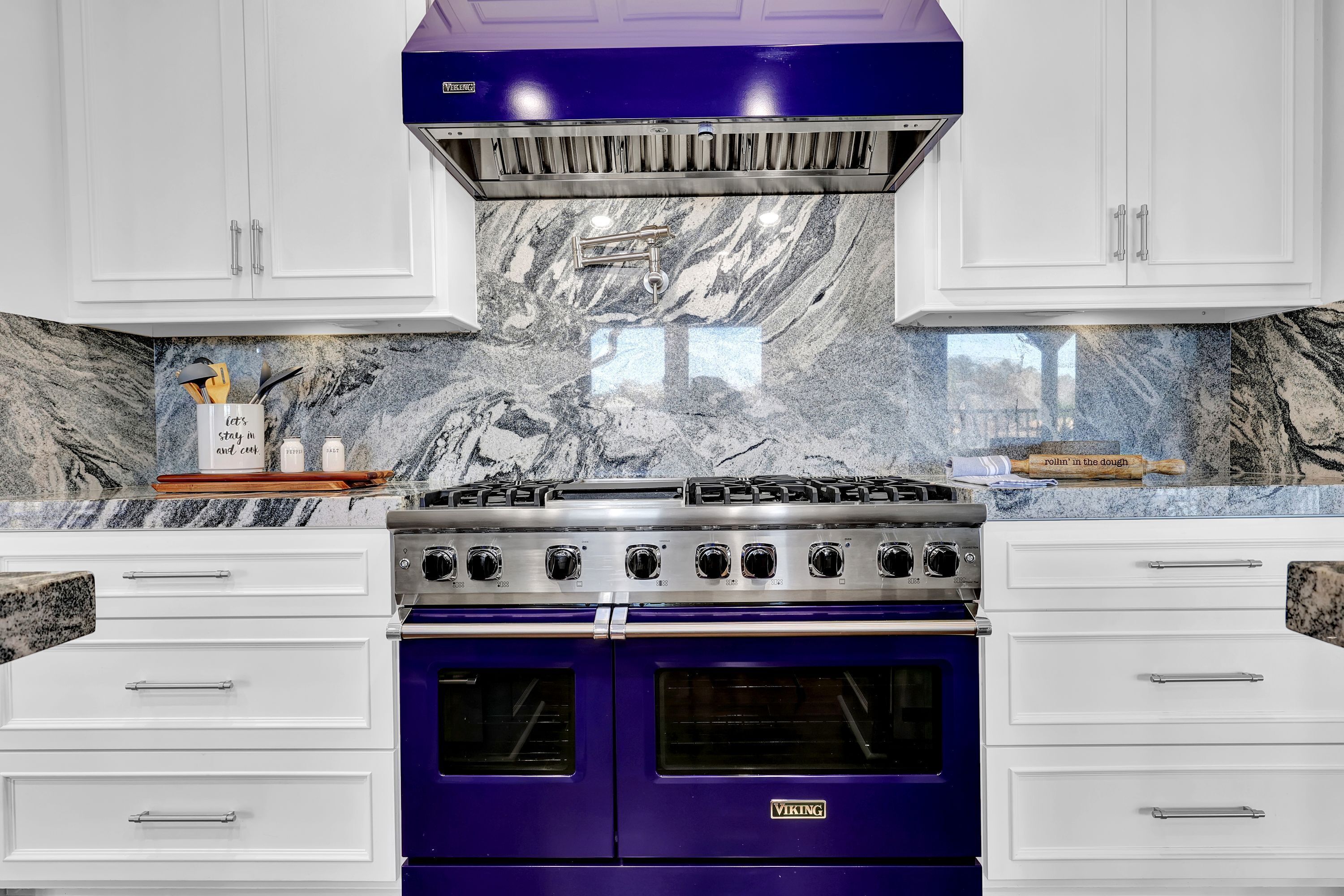 A kitchen with white cabinets, a blue Viking stove, and marble backsplash.