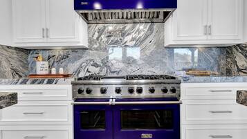 A kitchen with white cabinets, a blue Viking stove, and marble backsplash.