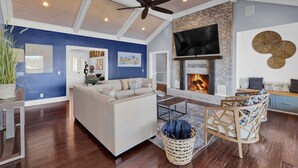 A spacious living room with a fireplace, a ceiling fan, and a TV mounted on the wall. - Private 7BR Lakehouse Estate Pool Hottub 13 Beds (Lizella)