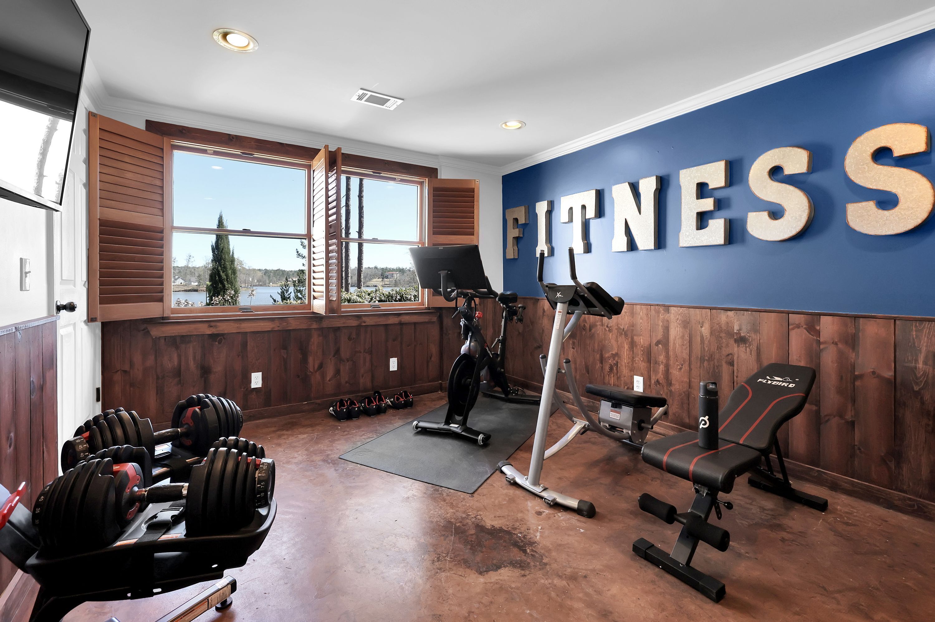 A gym with a large window, a wall with 'FITNESS' written on it, and various exercise equipment.