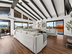 A spacious living room with a large sectional sofa, a coffee table, and a fireplace. There are large windows offering views of the surrounding area. - Lakefront House Golf Cart and Kayaks Included Dog Friendly West End of PCB (Panama City Beach)