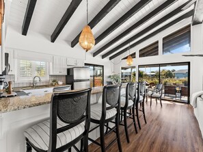 A modern kitchen with white cabinets, a stainless steel refrigerator, and a dining area with black chairs and a wooden table. - Lakefront House Golf Cart and Kayaks Included Dog Friendly West End of PCB (Panama City Beach)