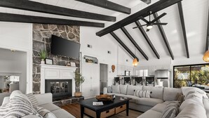Een moderne woonkamer met een stenen openhaard, een grote bank en een keuken op de achtergrond.