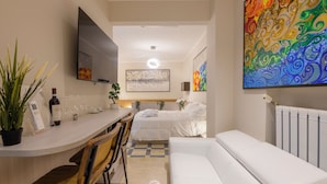 A modern hotel room with a bed, a sofa, a dining area with a table and chairs, a TV mounted on the wall, and a large abstract painting. - DibraLuxurySuites (Milan)