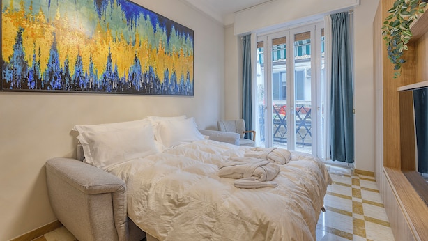 A hotel room with a large bed, a sofa, a painting on the wall, and a view of the outside through the window. - DibraLuxurySuites (Milan)