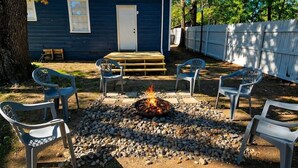 A backyard with a fire pit surrounded by chairs, a wooden deck, and a blue building. - Waggoner in Longview (Longview)