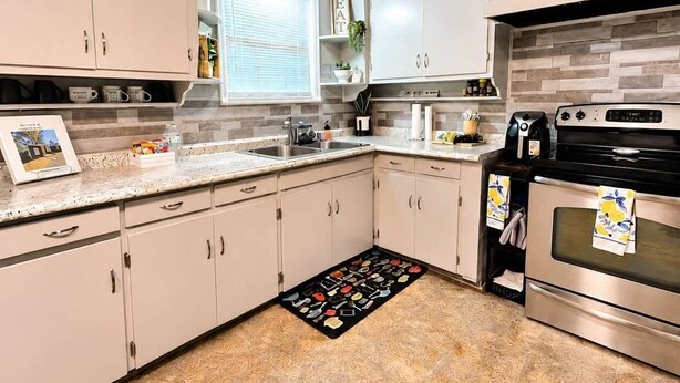 A modern kitchen with light-colored cabinets, a granite countertop, a built-in oven, and a backsplash with a gray and white pattern. - Waggoner in Longview (Longview)