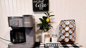 A coffee station with a Keurig coffee maker, a coffee-themed sign, a jar of sugar, a jar of cream, and a basket of coffee pods. - Waggoner in Longview (Longview)